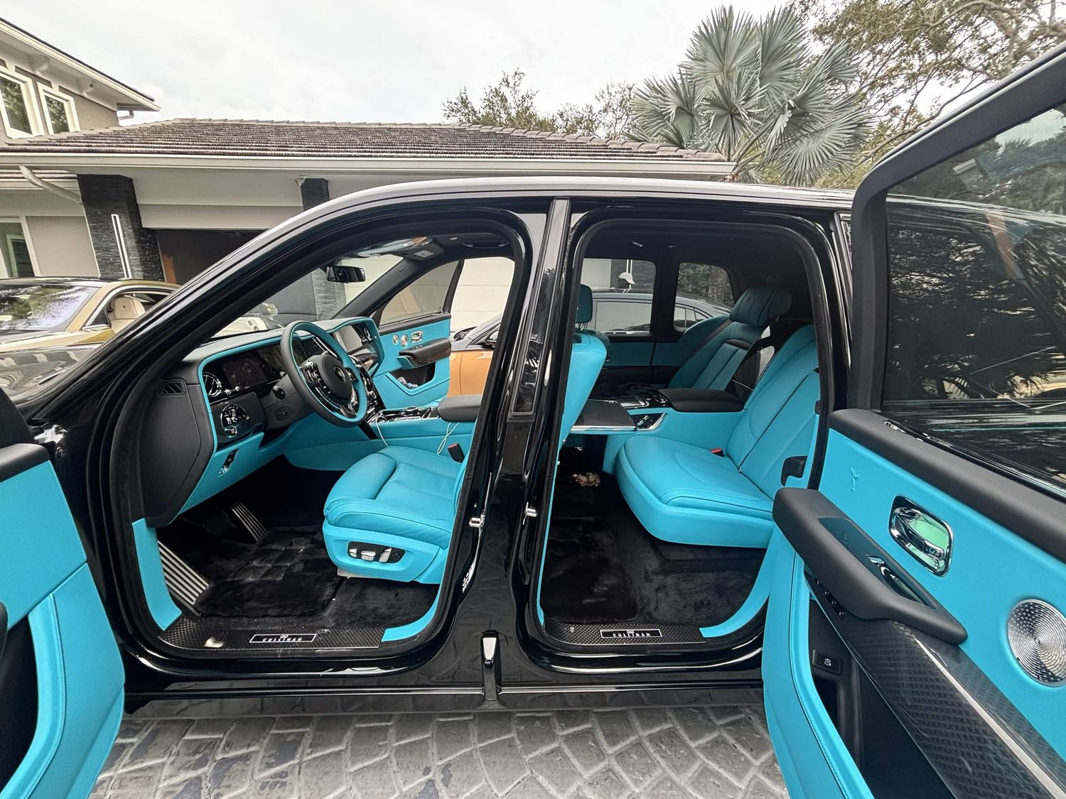 Interior of a black Rolls-Royce Cullinan with turquoise leather, doors open, tinted glass