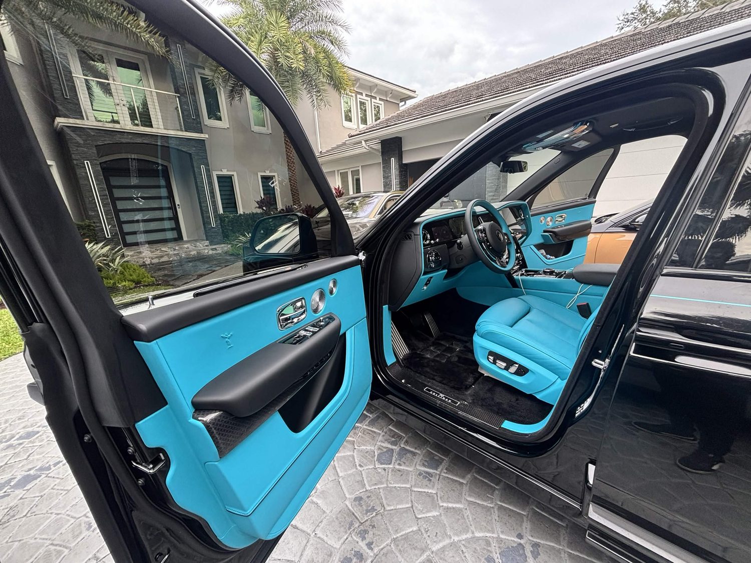 Open driver door of a black Cullinan showing turquoise door panel